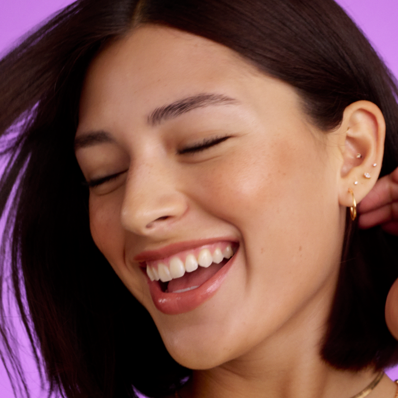 Woman with big smile with hand in her hair on purple background