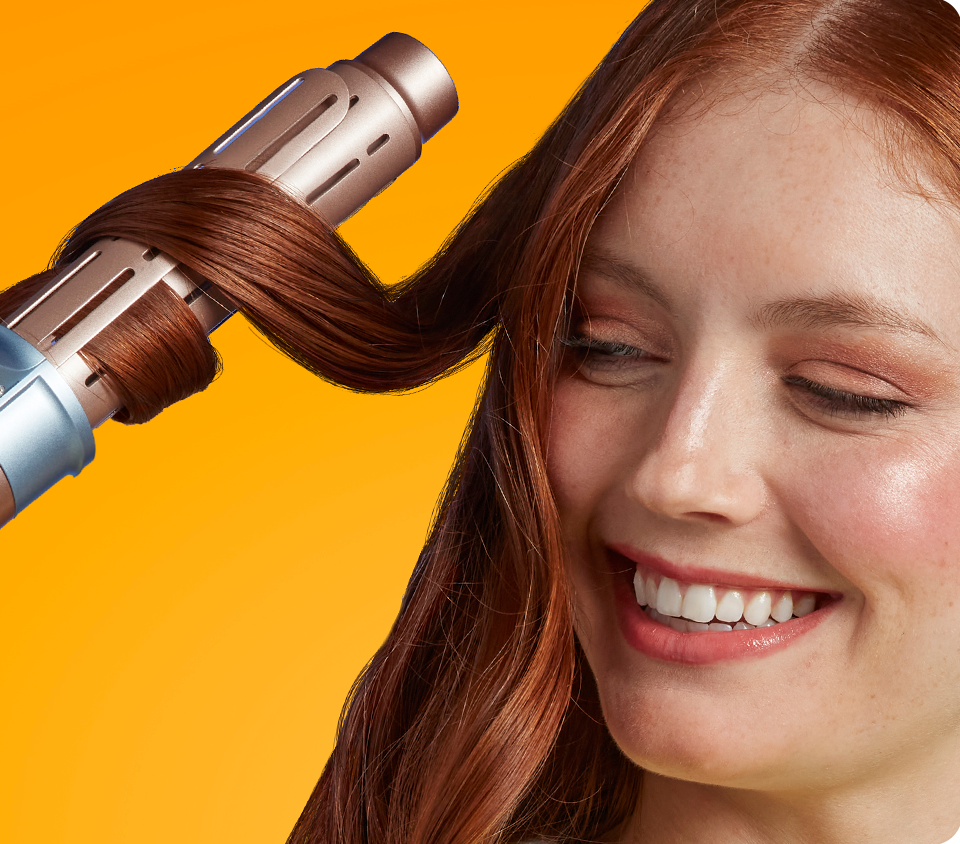 Woman using Conair curling iron to curl long, straight hair, against yellow background