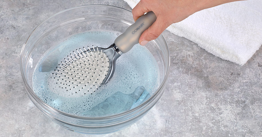 Soaking a hairbrush in a bowl of warm soapy water.