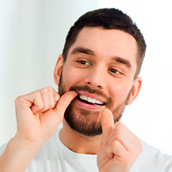 Hombre limpiándose los dientes con hilo dental