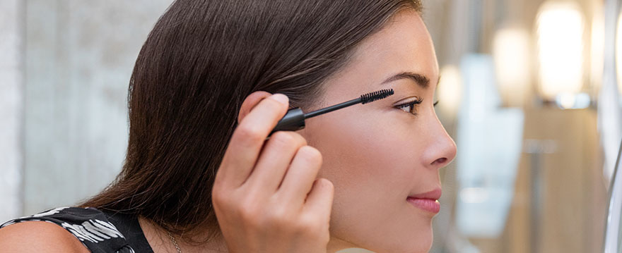 Pretty woman applying mascarra in mirror.