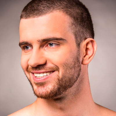 Man smiling in the mirror with beard stubble freshly groomed.